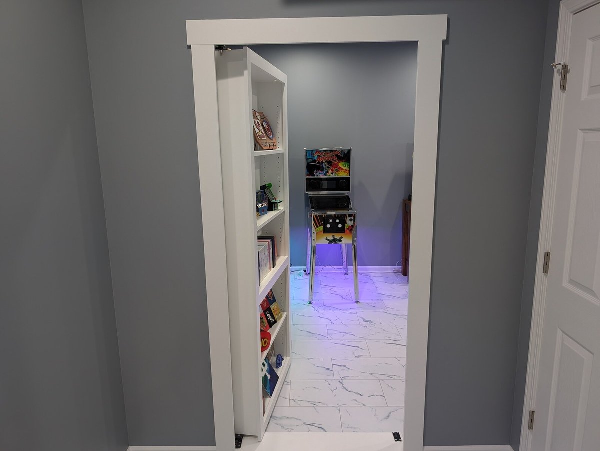 Secret bookshelf door opening into a brightly lit game room during a basement remodel by Clear Contractors in Northwest Indiana