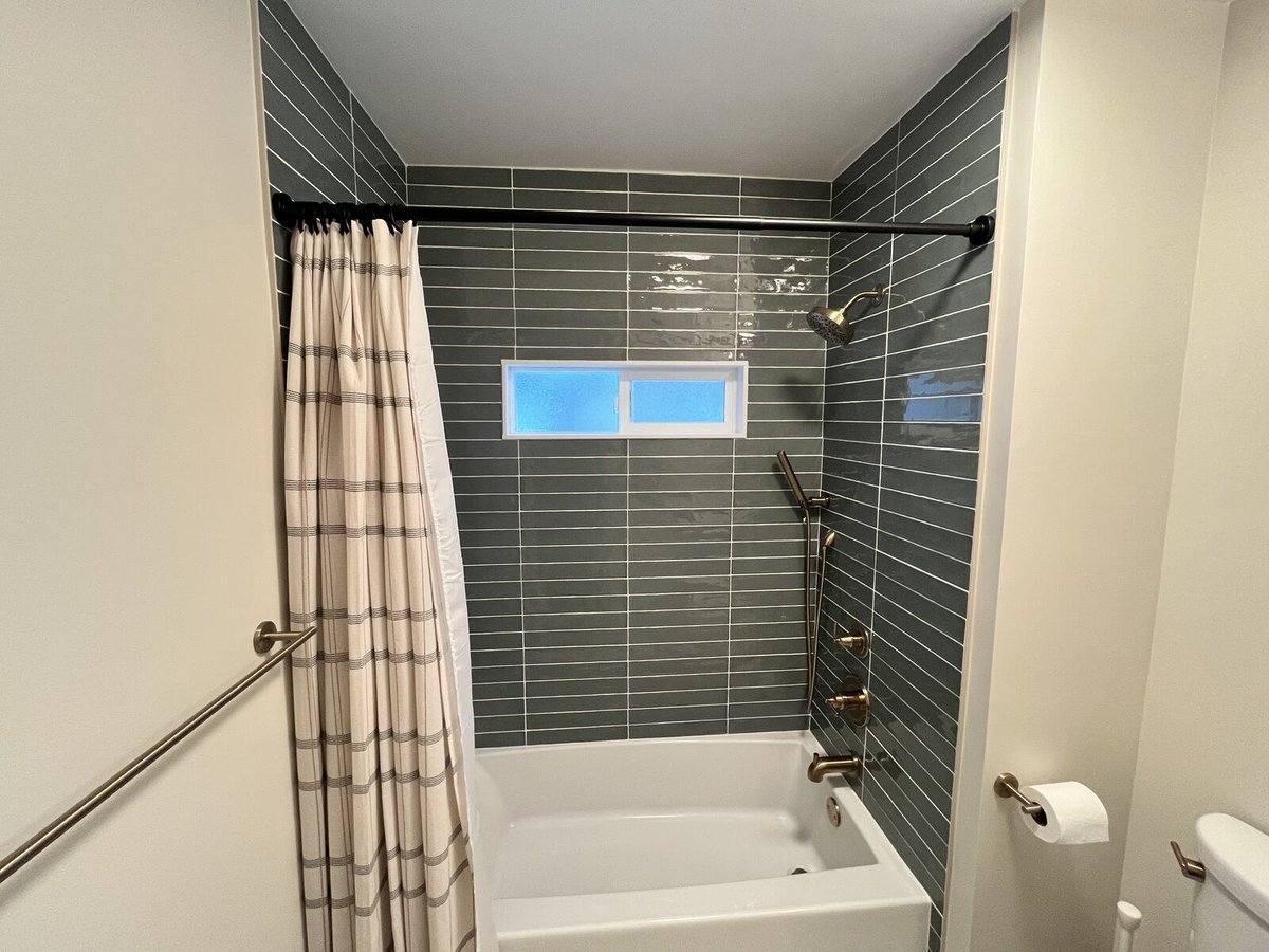 Bathroom remodel featuring a tub and shower with green tiles and gold hardware, completed by Clear Contractors in Northwest Indiana