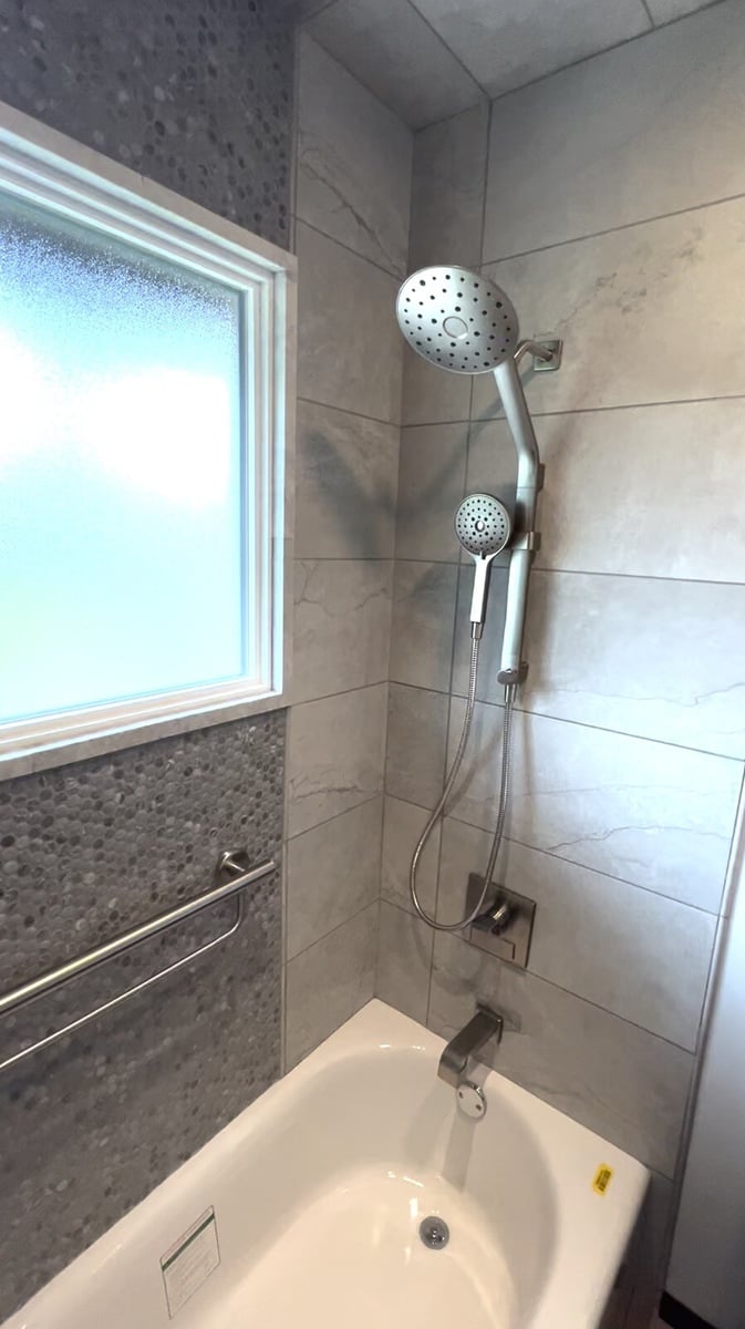 Modern bathroom shower with gray tiles and a frosted window, featuring a handheld showerhead, remodeled by Clear Contractors in Northwest Indiana