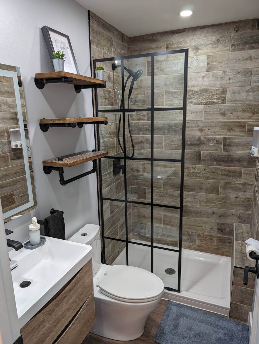 Modern bathroom remodel with wood-style tile walls, glass shower enclosure, and industrial shelves by Clear Contractors in Northwest Indiana