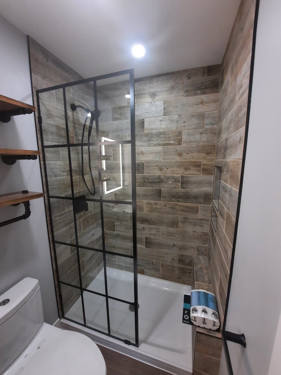 Walk-in shower with a black-framed glass door and wood-textured tiles, part of a modern bathroom remodel