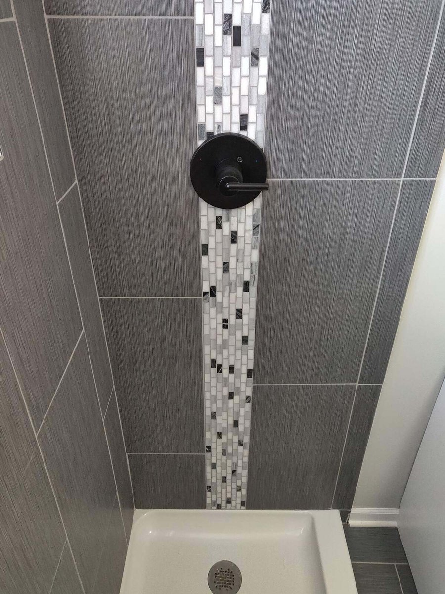 Close-up of gray tiled shower with mosaic accent strip and matte black fixtures by Clear Contractors in Northwest Indiana